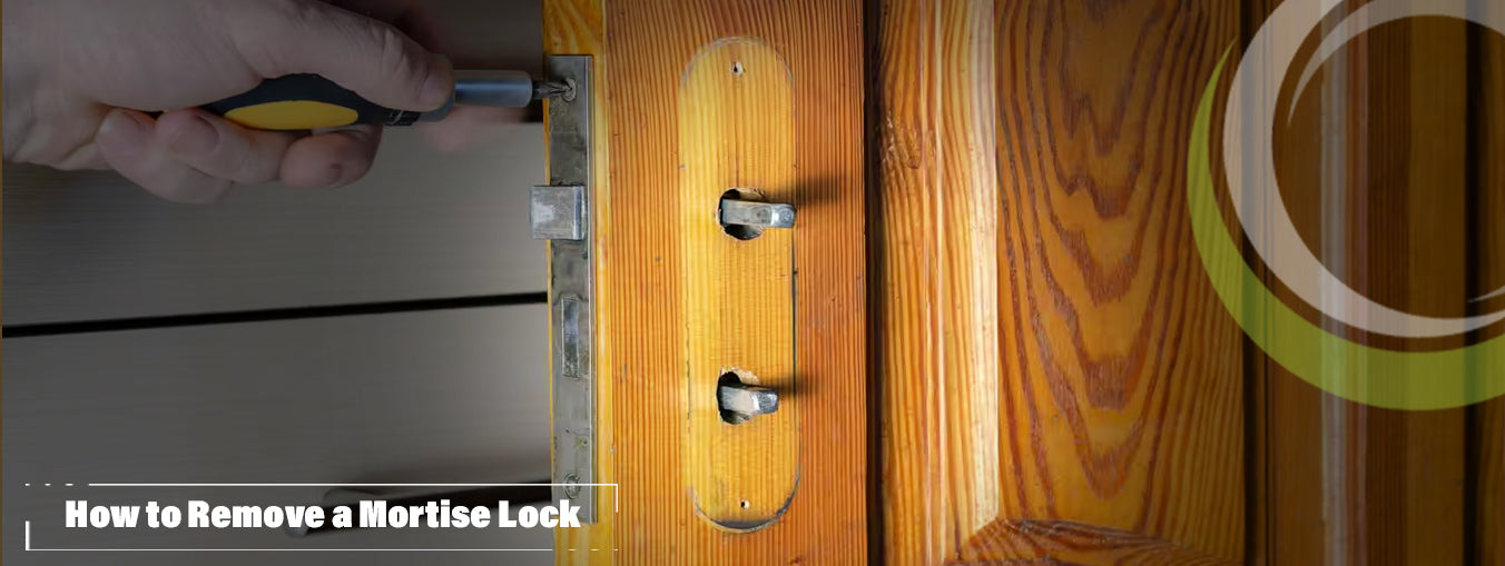 Removing a mortise lock from a wood door using a screwdriver.