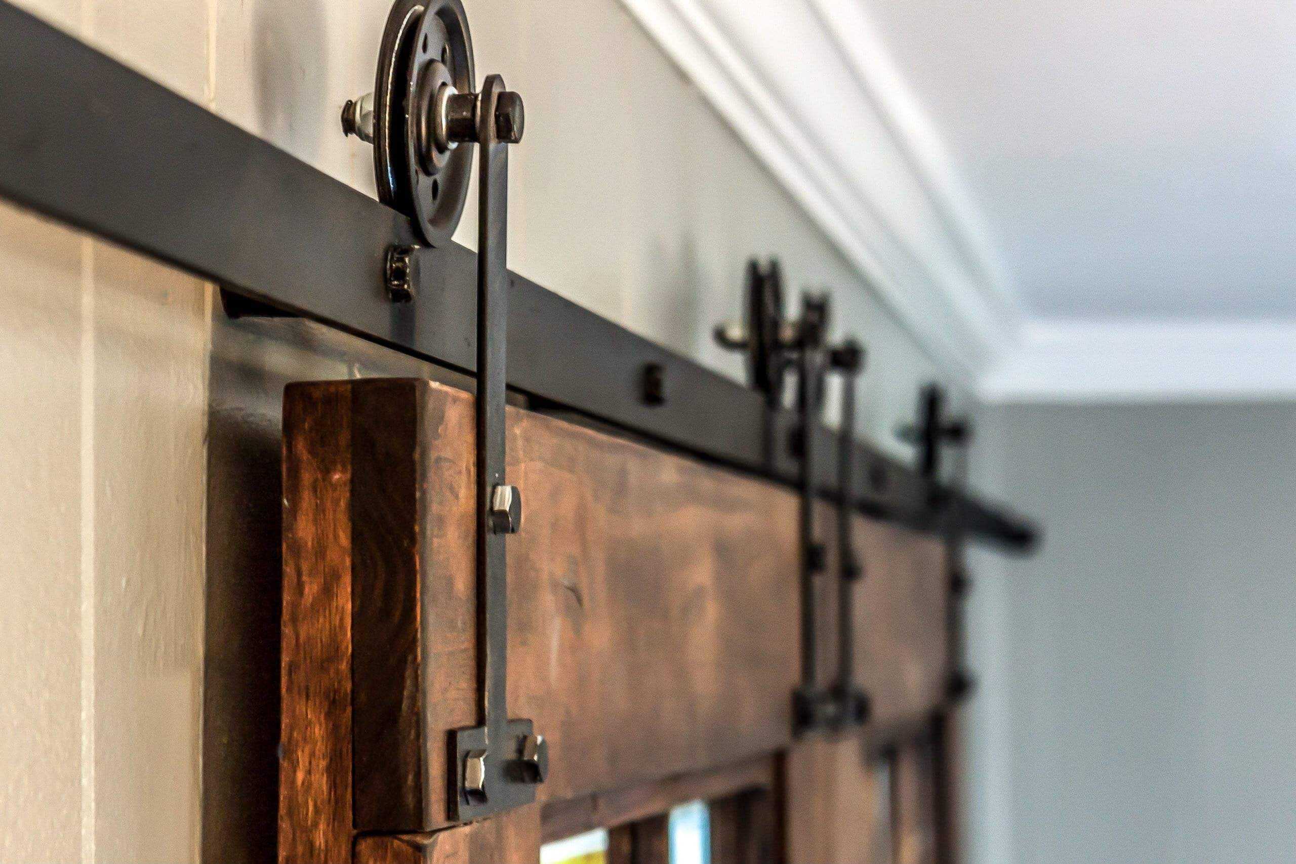 Dark brown wood sliding barn door hardware detail; black metal track and rollers.