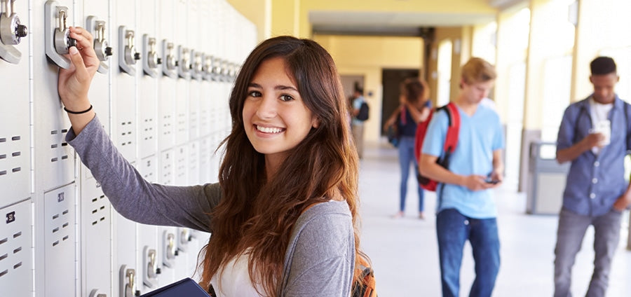 Smiling high school student opening locker in hallway.